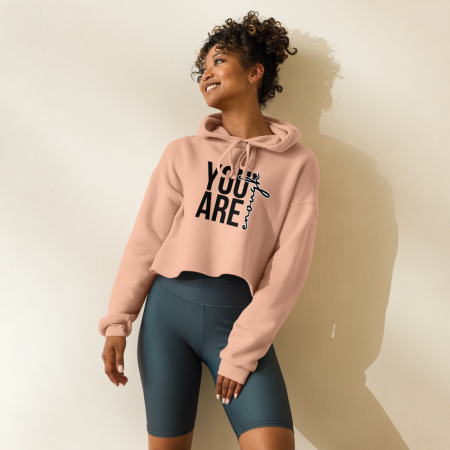 Woman wearing cropped hoodie with you are enough cropped hoodie print, leaning against beige wall
